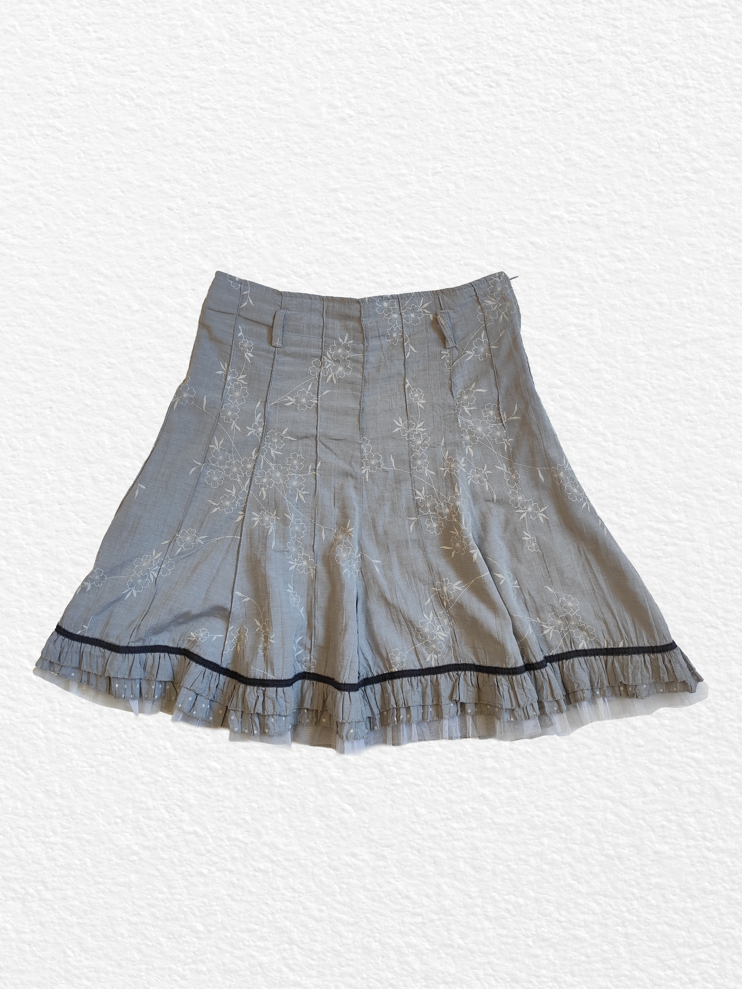 Jupe plissée grise avec motif floral et bordure noire.