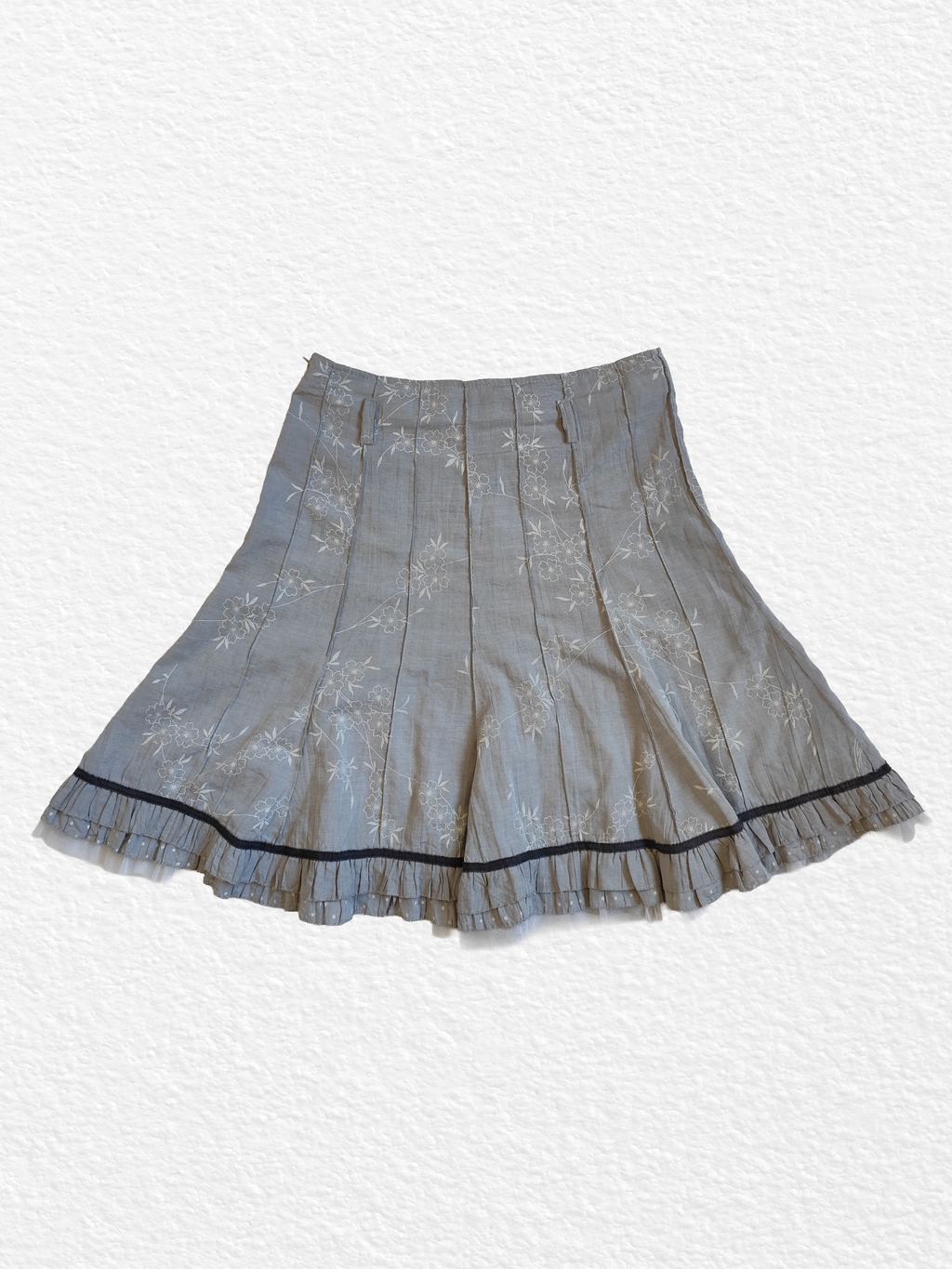 Jupe plissée grise avec motif floral et bordure noire.