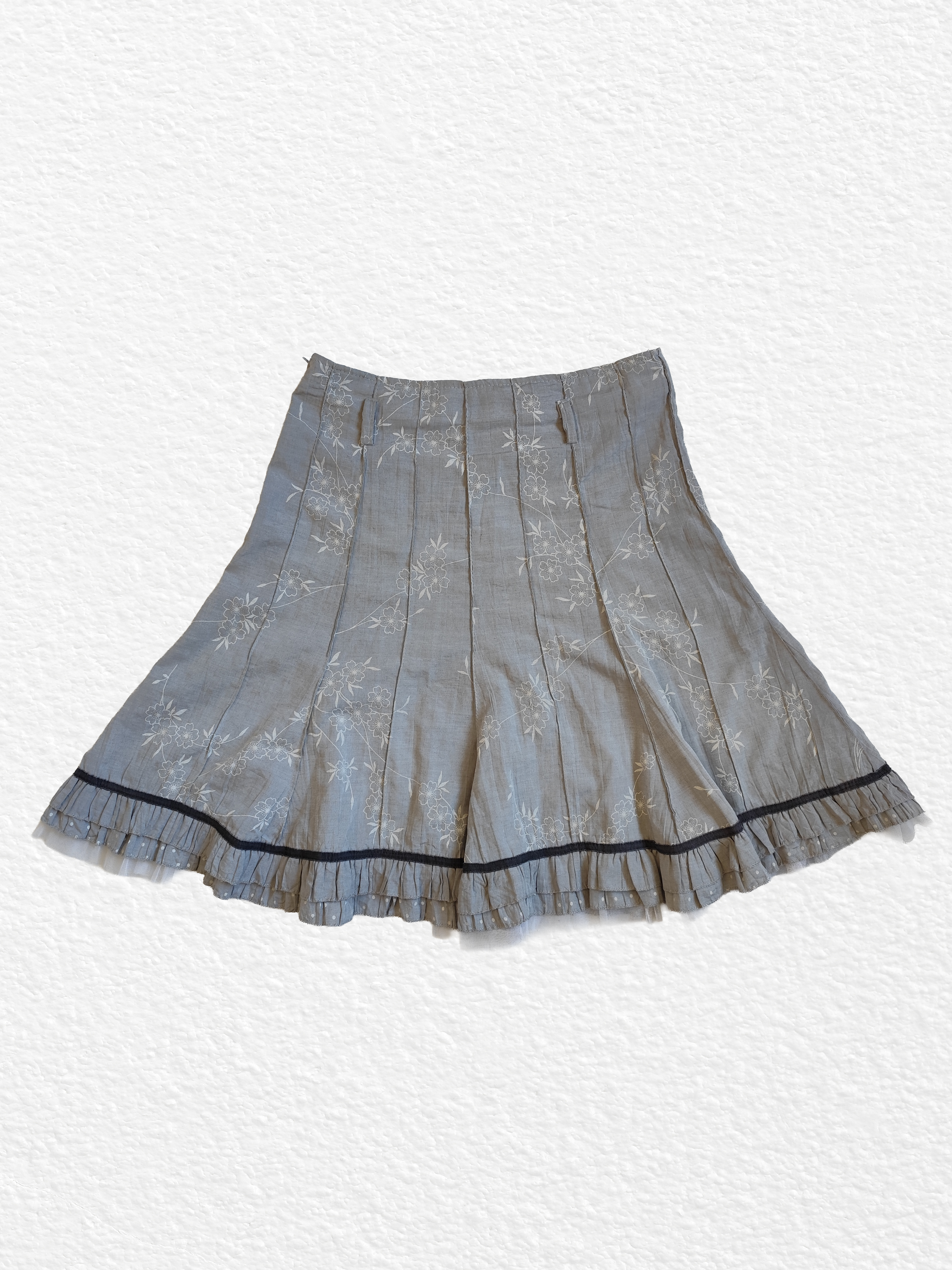 Jupe plissée grise avec motif floral et bordure noire.